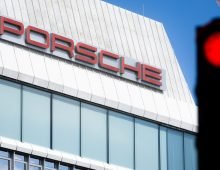 A traffic light is glowing red in front of the Porsche logo on a building at the company's headquarters in Stuttgart-Zuffenhausen. Photo: Christoph Schmidt/dpa
